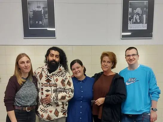 5 Mitglieder des Teams stehen vor einer Wand mit Fotos