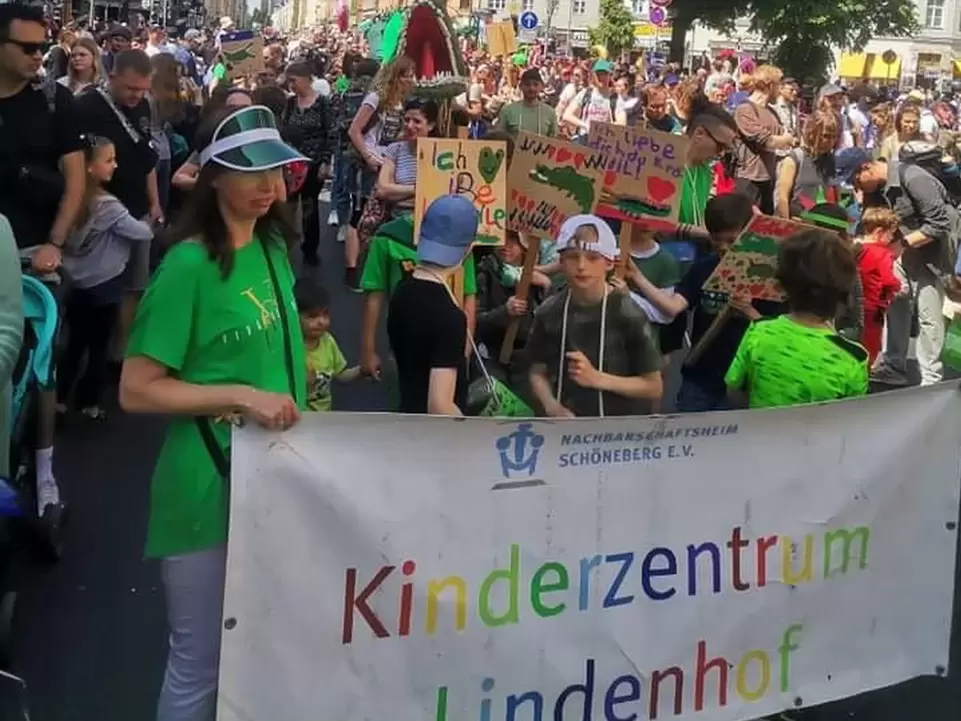 Kinder tragen ein gro&szlig;es Banner mit der Aufschrift "Kinderzentrum Lindenhof" vor einer gro&szlig;en Menschenansammlung