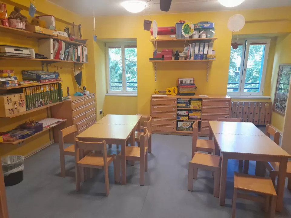 Zimmer mit gelben W&auml;nden und B&uuml;cherregalen, in der Mitte stehen zwei Tische mit kleinen St&uuml;hlen