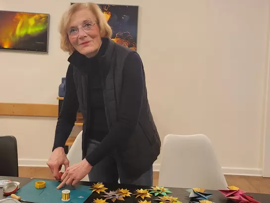 Eine Frau steht am Tisch und zeigt ihre gefalteten Weihnachtsterne