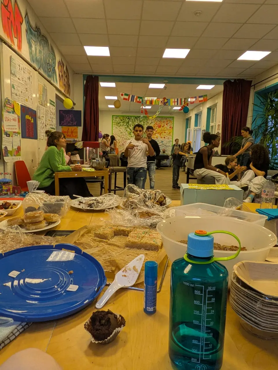 Zu sehen sind verschiedene KInder und Jugendliche sowie erwachsene im Hauptraum vom Flipperklub. An der Seite steht eine Popcorn Maschine und im Raum eine Tischtennisplatte. 
