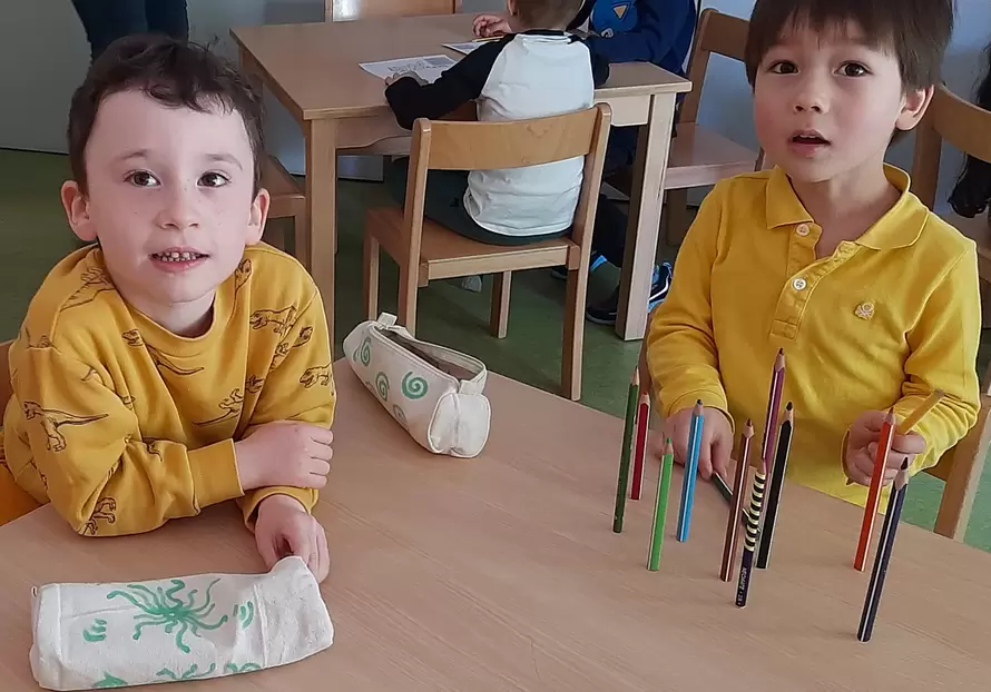 Zwei Kinder sitzen an einem Tisch, mit Buntstiften und selbst bemalten Stiftm&auml;ppchen