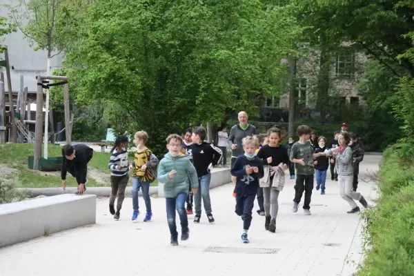 Kinder rennen einen Weg entlang, links ist der Spielplatz zu erkennen