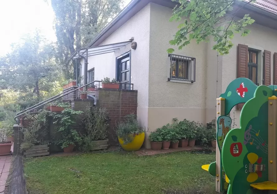 graues Haus mit Vorgarten und B&auml;umen im Hintergrund