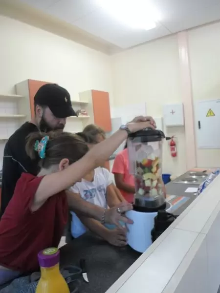 Kinder stehen mit einem P&auml;dagogen in der K&uuml;che um einen Mixer mit Obst