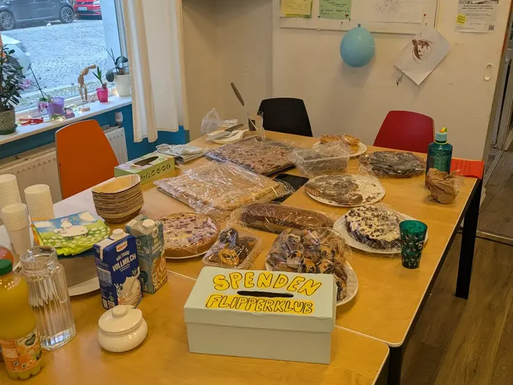 Bild von einem Tisch im Flipperklub mit verschiedenen Kuchen darauf und einer blauen Spendenbox