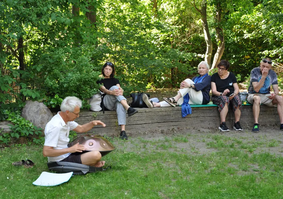 Ein Mann sitzt auf dem Rasen und spielt die Handpan vor ein paar Zuschauern