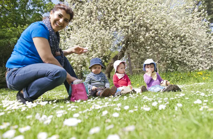 Eine Frau sitzt mit drei kleinen Kindern auf einer Wiese